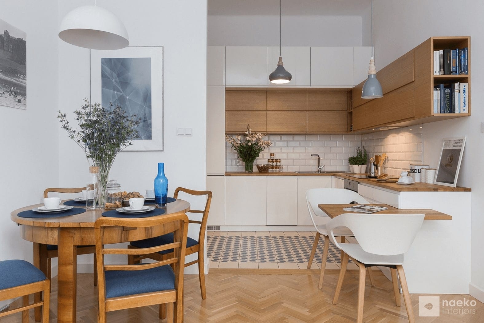 Projekt kuchni w stylu skandynawskim z białą zabudową i drewnianymi elementami oraz starym stołem i krzesłami w stylu vintage i granatowymi dodatkami